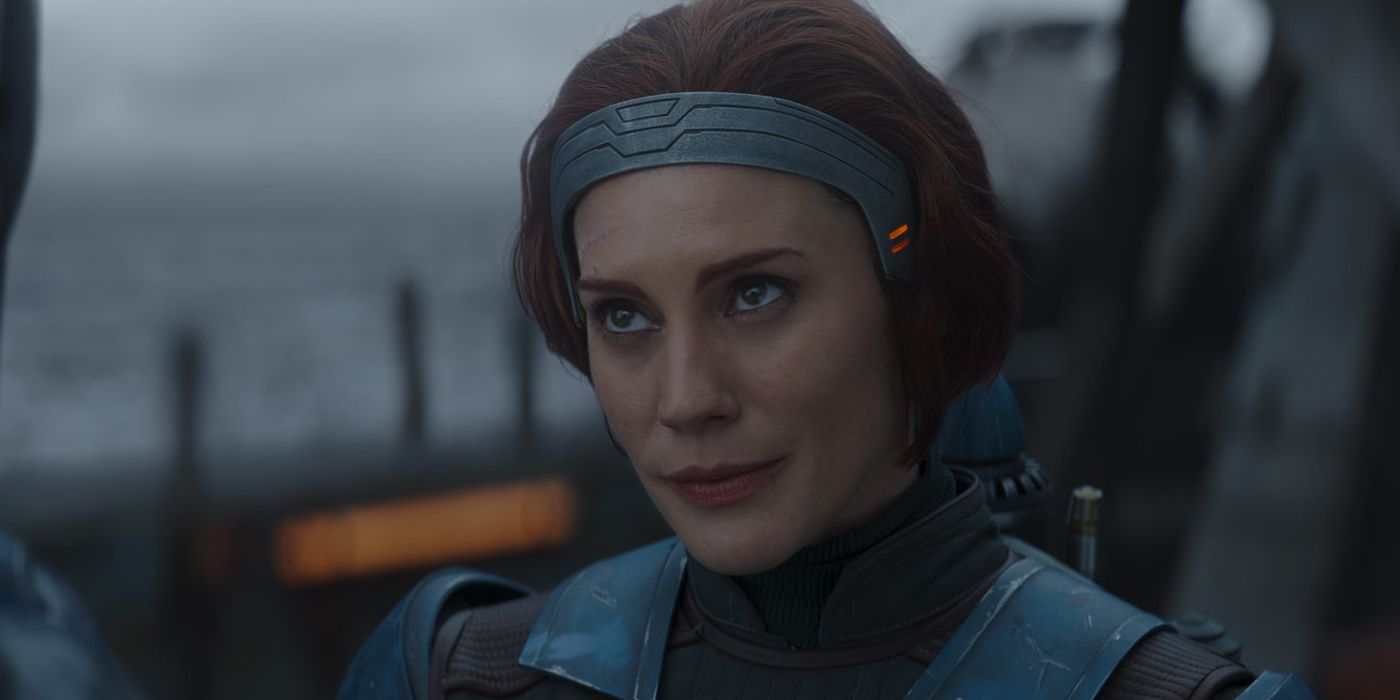 Bo-Katan Kryze stands talking to Din Djarin, removing his helmet.