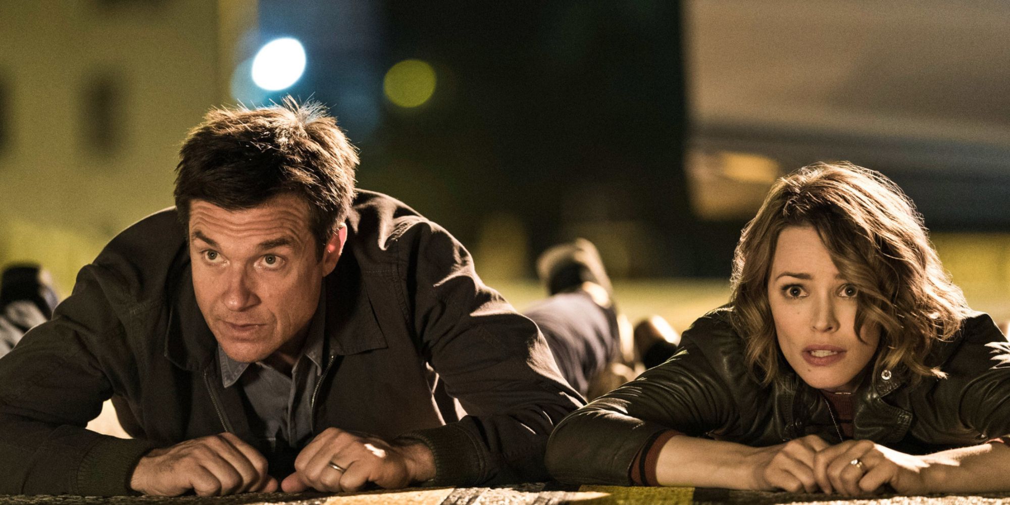 Jason Bateman and Rachel McAdams lie on the ground looking scared. 