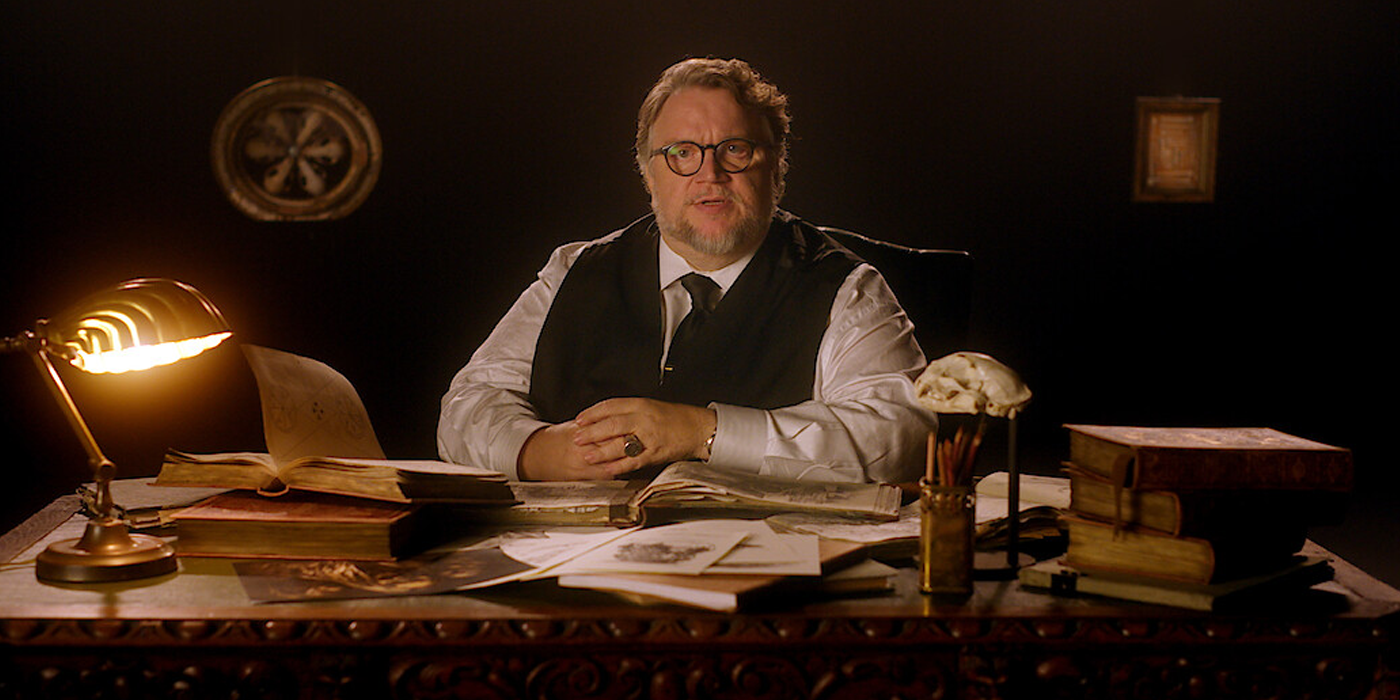Guillermo del Toro sits at a table and talks to the camera.