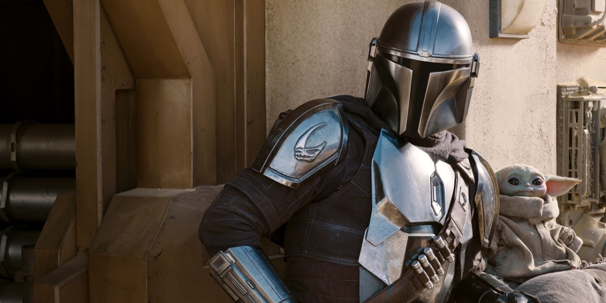The Mandalorian and Grog stand against a wall in The Mandalorian.