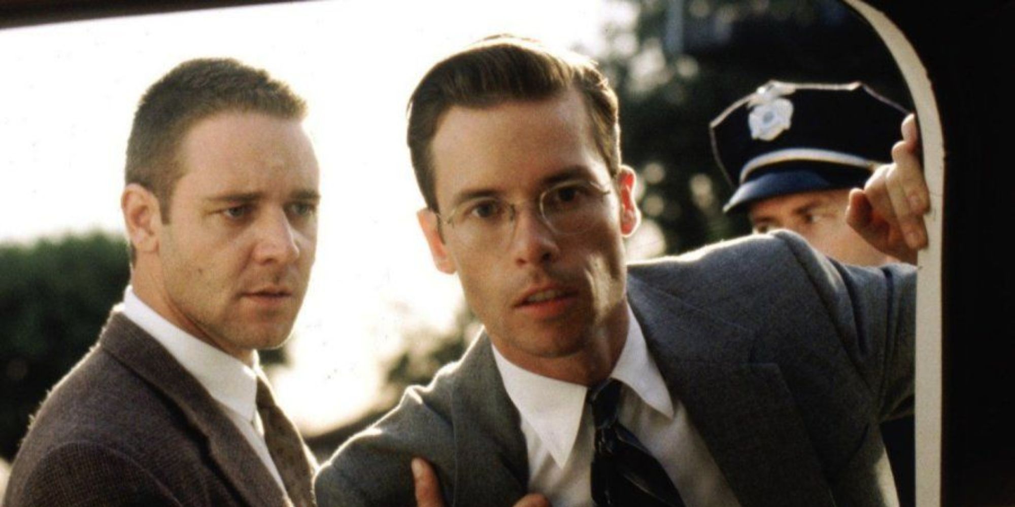 Russell Crowe stands next to Guy Pearce looking into a car in LA Confidential. 