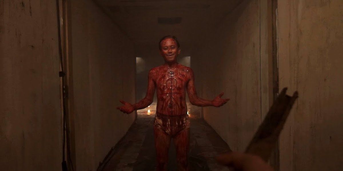 Shot from videotape 2: a smiling man stands in the corridor, covered in blood, with a carving on his chest.
