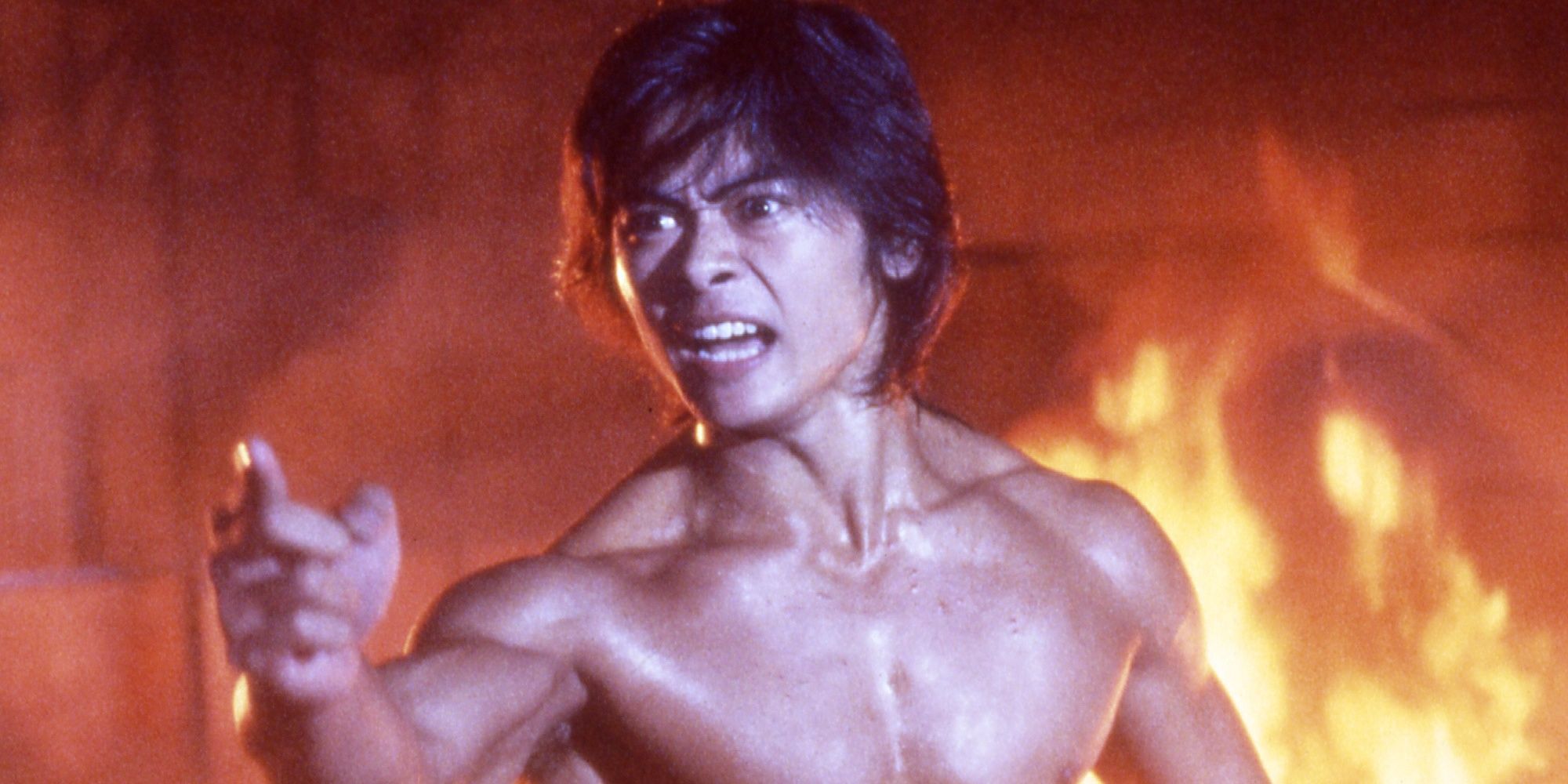 Shirtless man standing in front of a fire