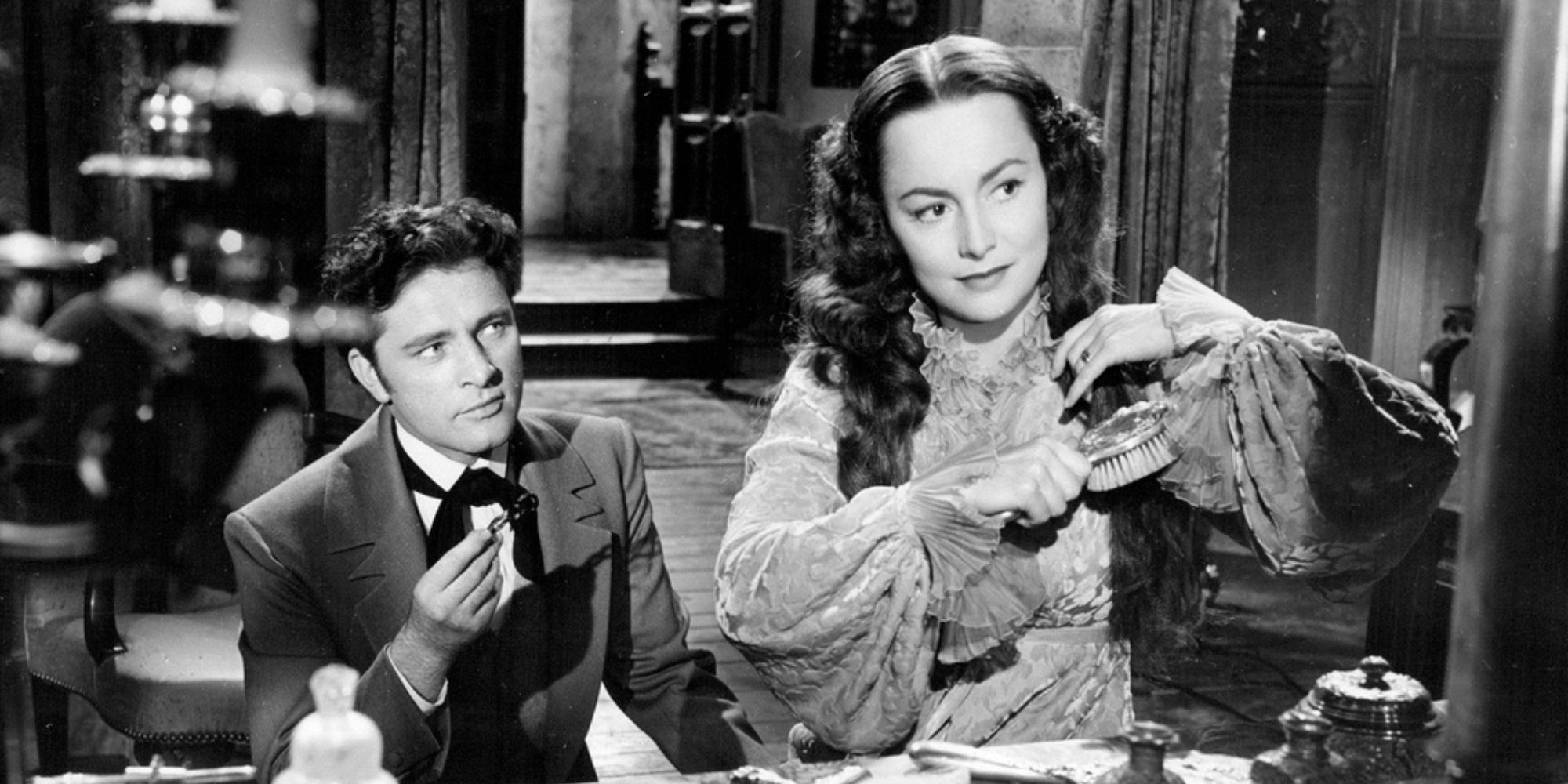 Richard Burton sits behind Olivia de Havilland and watches her brush her hair at her dressing table in My Cousin Rachel. 