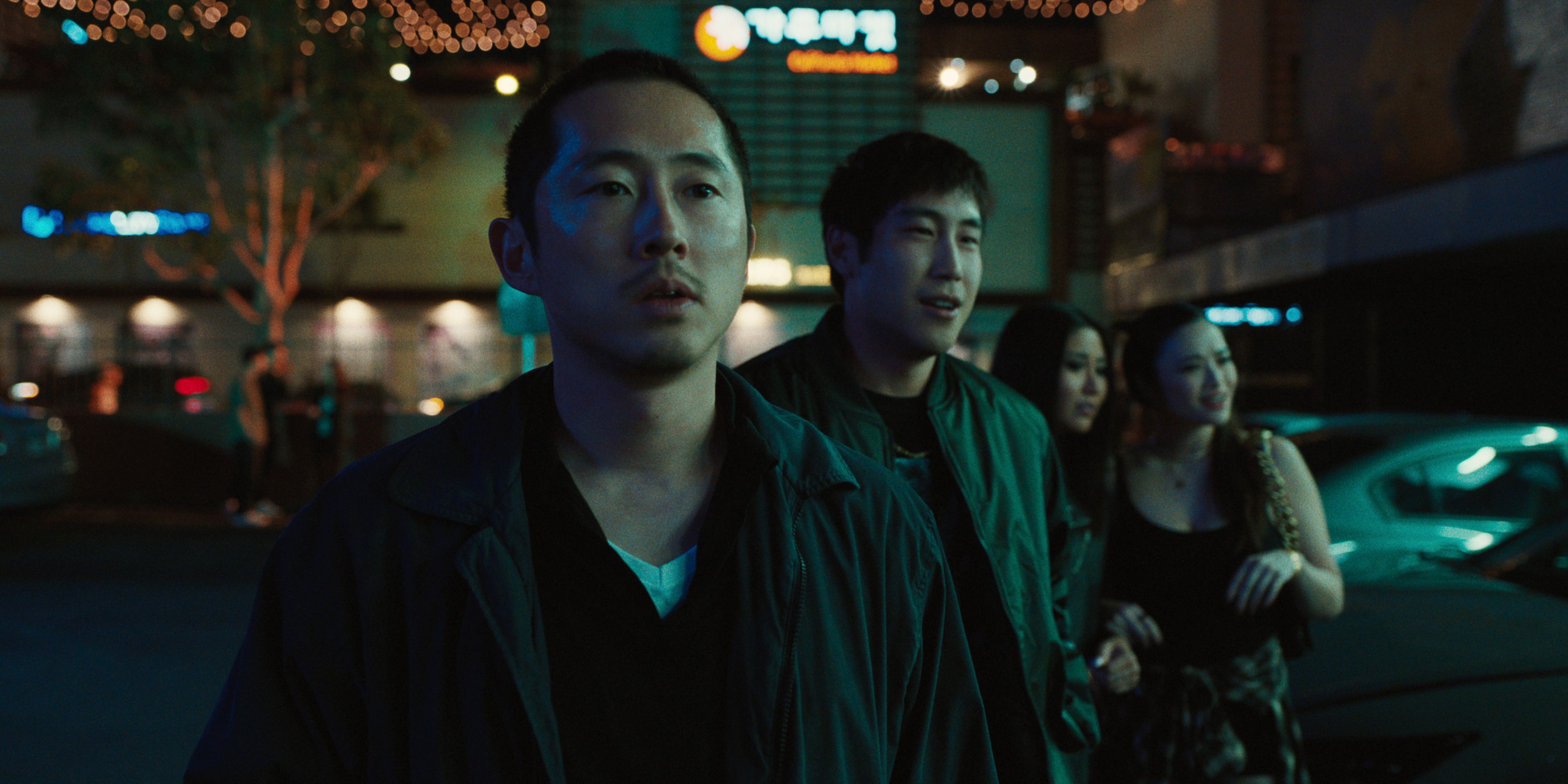 Steven Yeun as Danny Cho stands outside at night with a group of friends looking at something in the distance in BEEF.