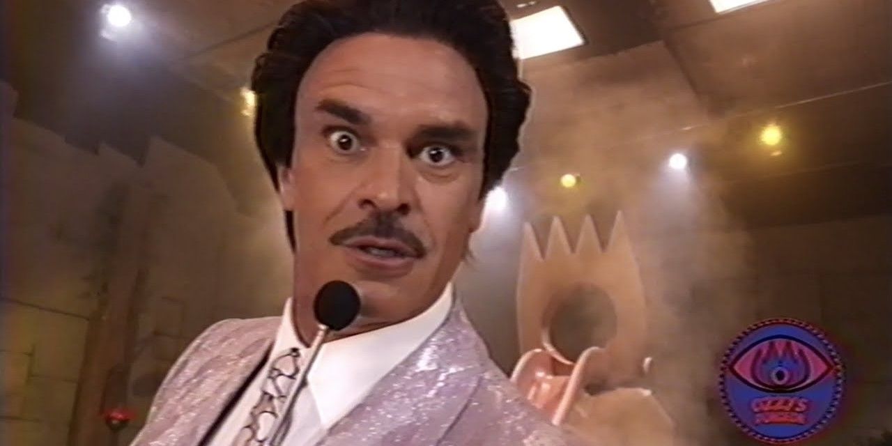 The game show host (Stephen Ogg) looks directly into the camera.