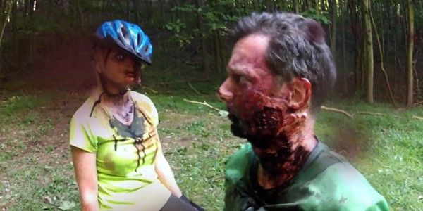 Two zombies, one with a bicycle helmet, are standing in the forest at V/H/S/2.