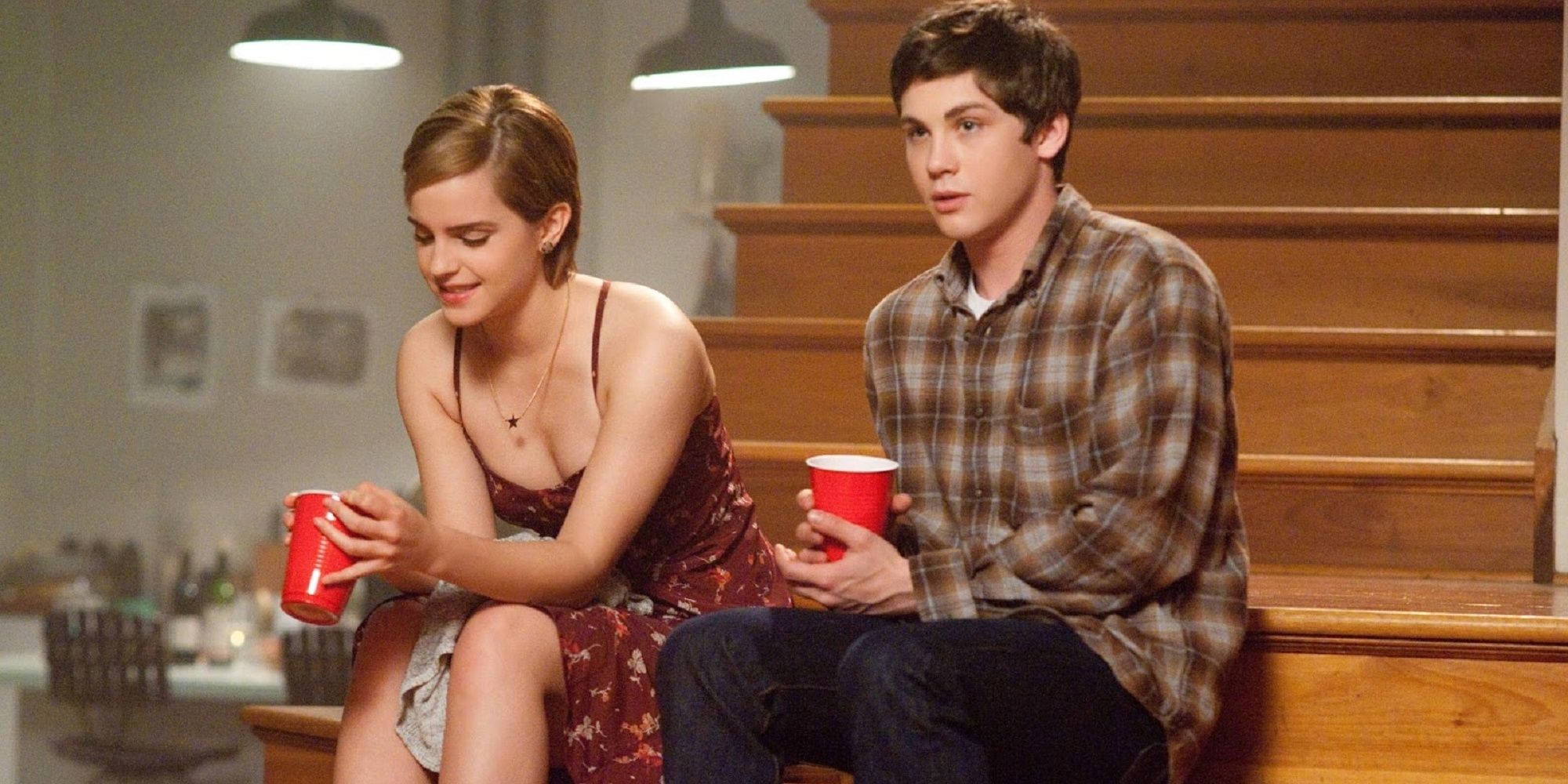 Emma Watson and Logan Lerman sit on the stairs at a party.