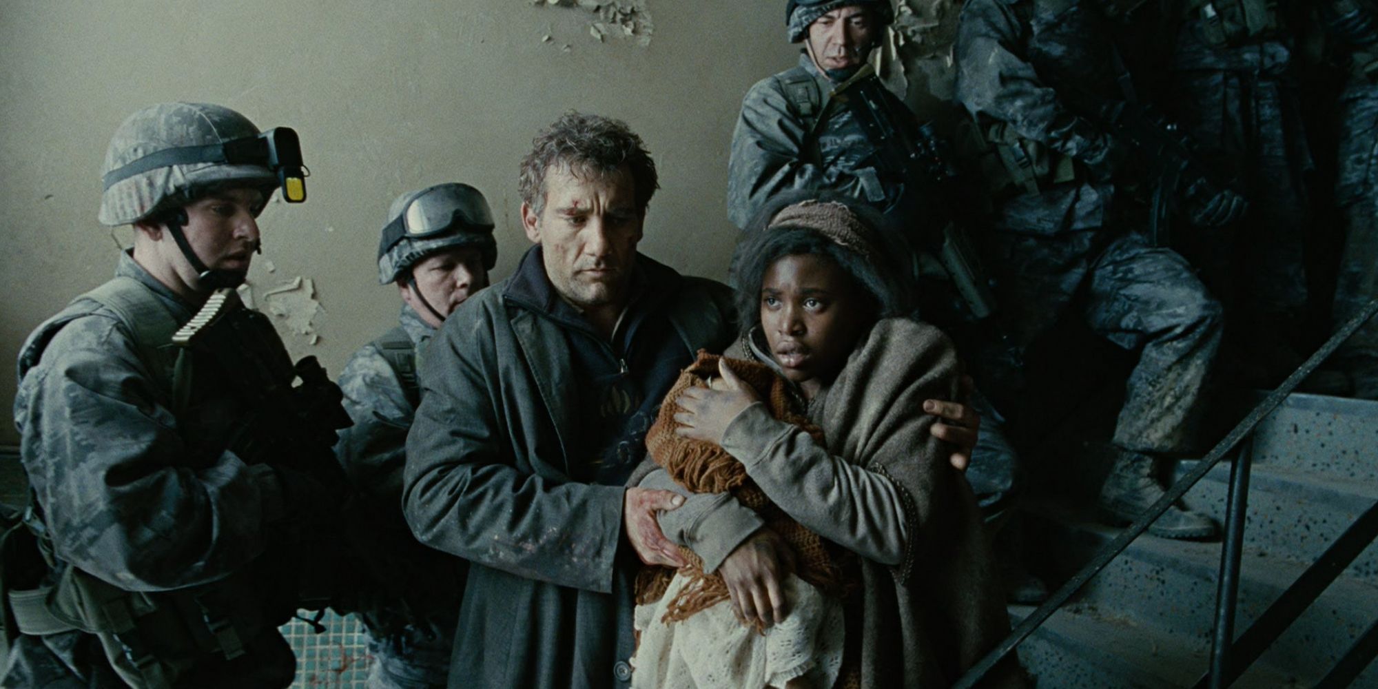 Theo (Clive Owen) and Key (Claire-Hope Ashiti) walk past soldiers with a baby in Children of Men (2006)