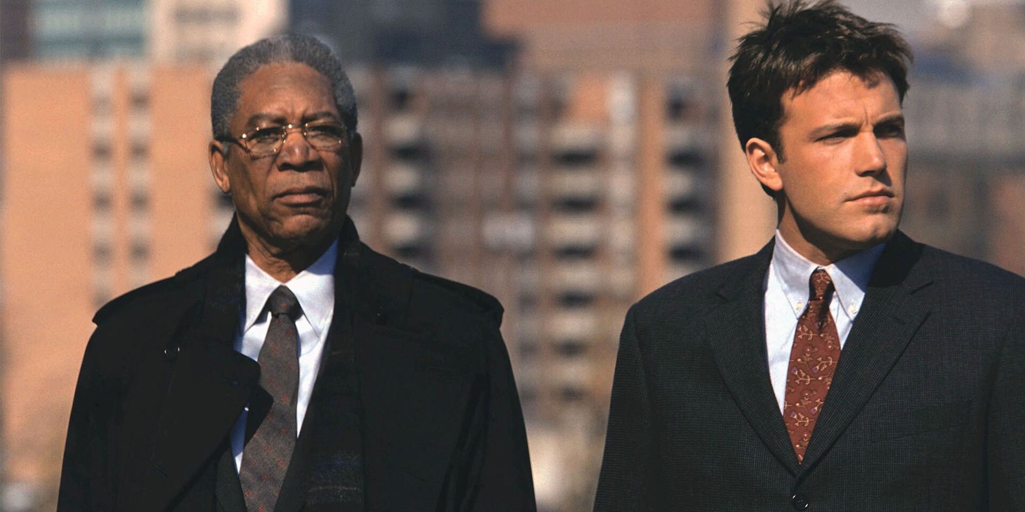 two men in suits stand on the roof of a building against the backdrop of the city