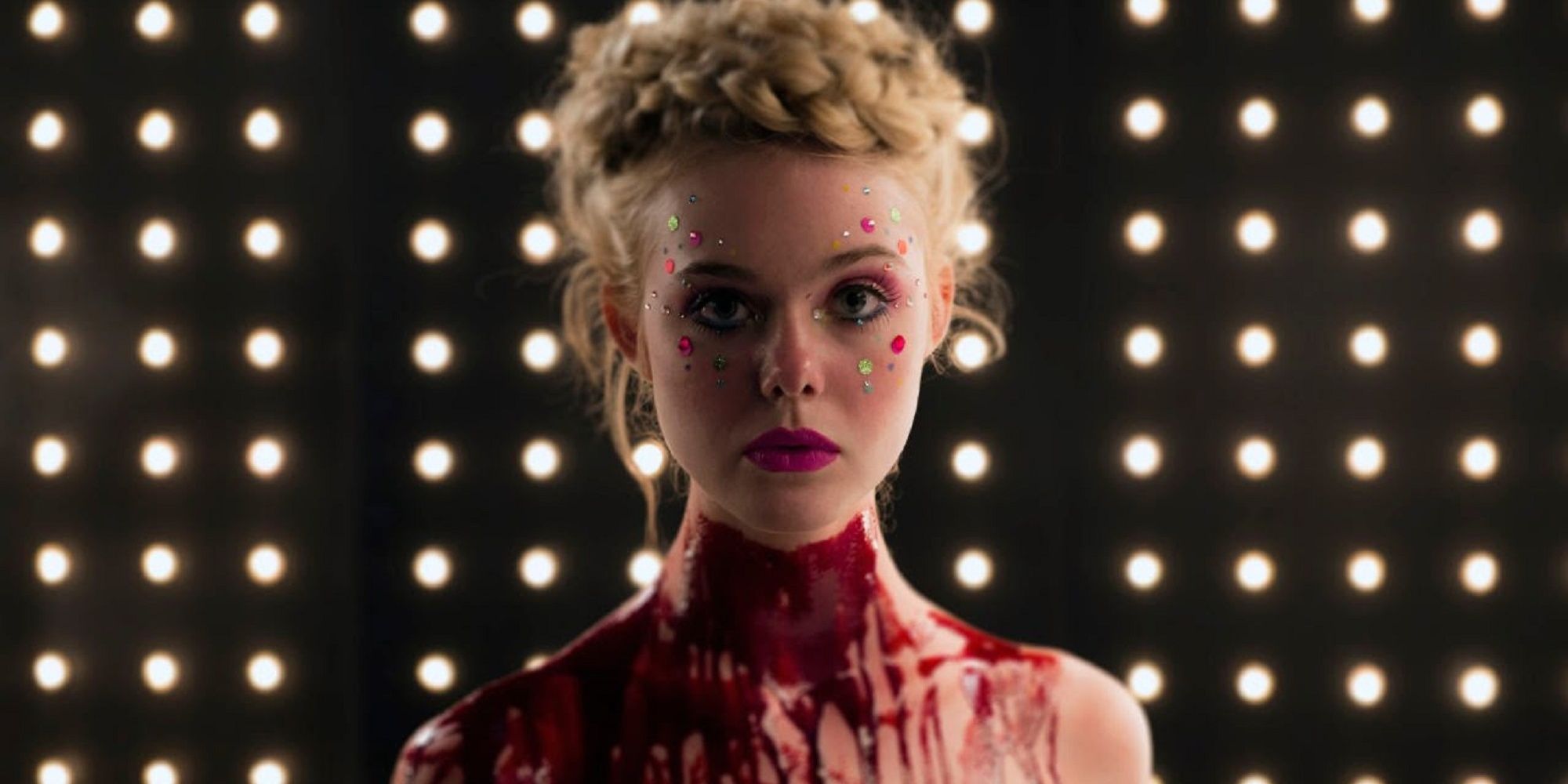 Elle Fanning stands in front of an illuminated backdrop with blood on her neck in The Neon Demon.