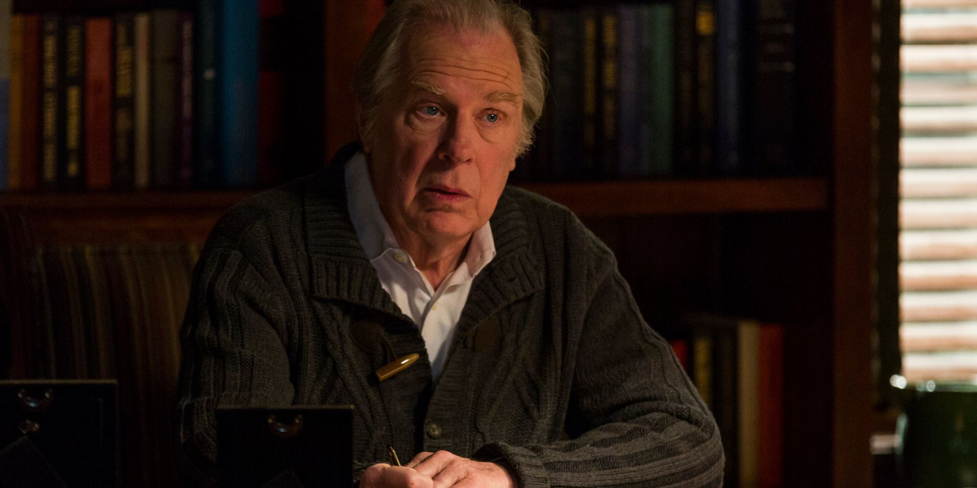 Michael McKean as Chuck McGill is seated at his desk in front of a bookshelf in Better Call Saul.