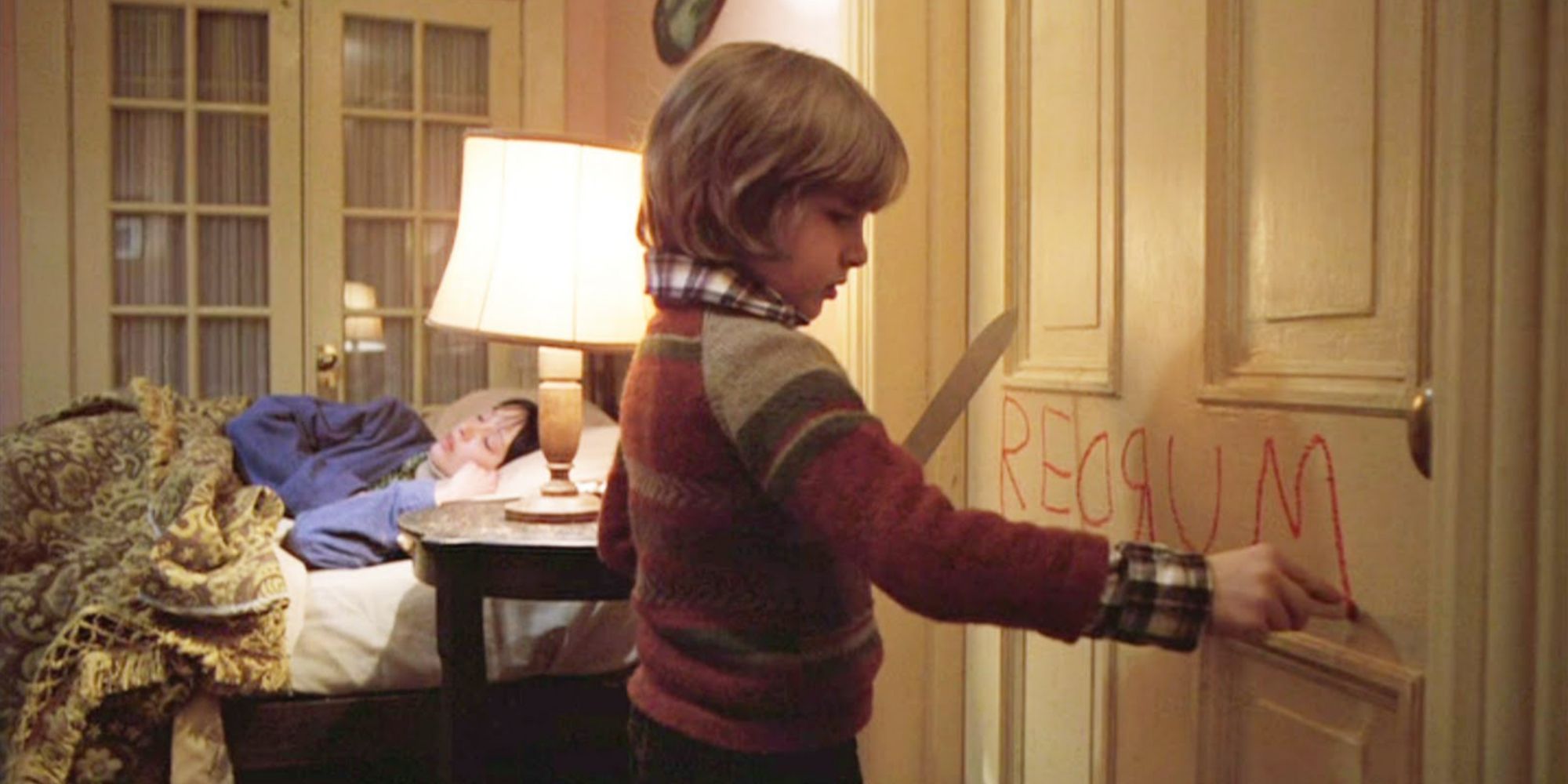 the boy writes a drum on the door while holding a knife: the mother is sleeping in bed in the background
