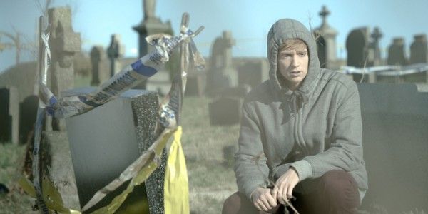 Kieran kneels before the grave in the flesh